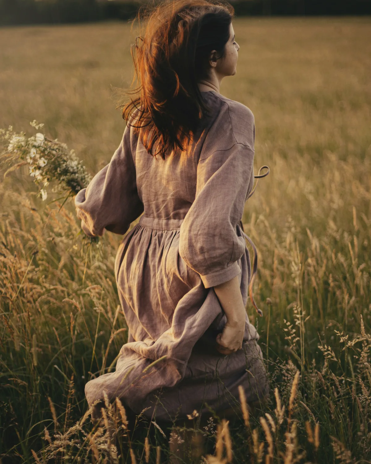 Mujer con vestido de lino caminando por un campo de hierba alta al atardecer, de espaldas
