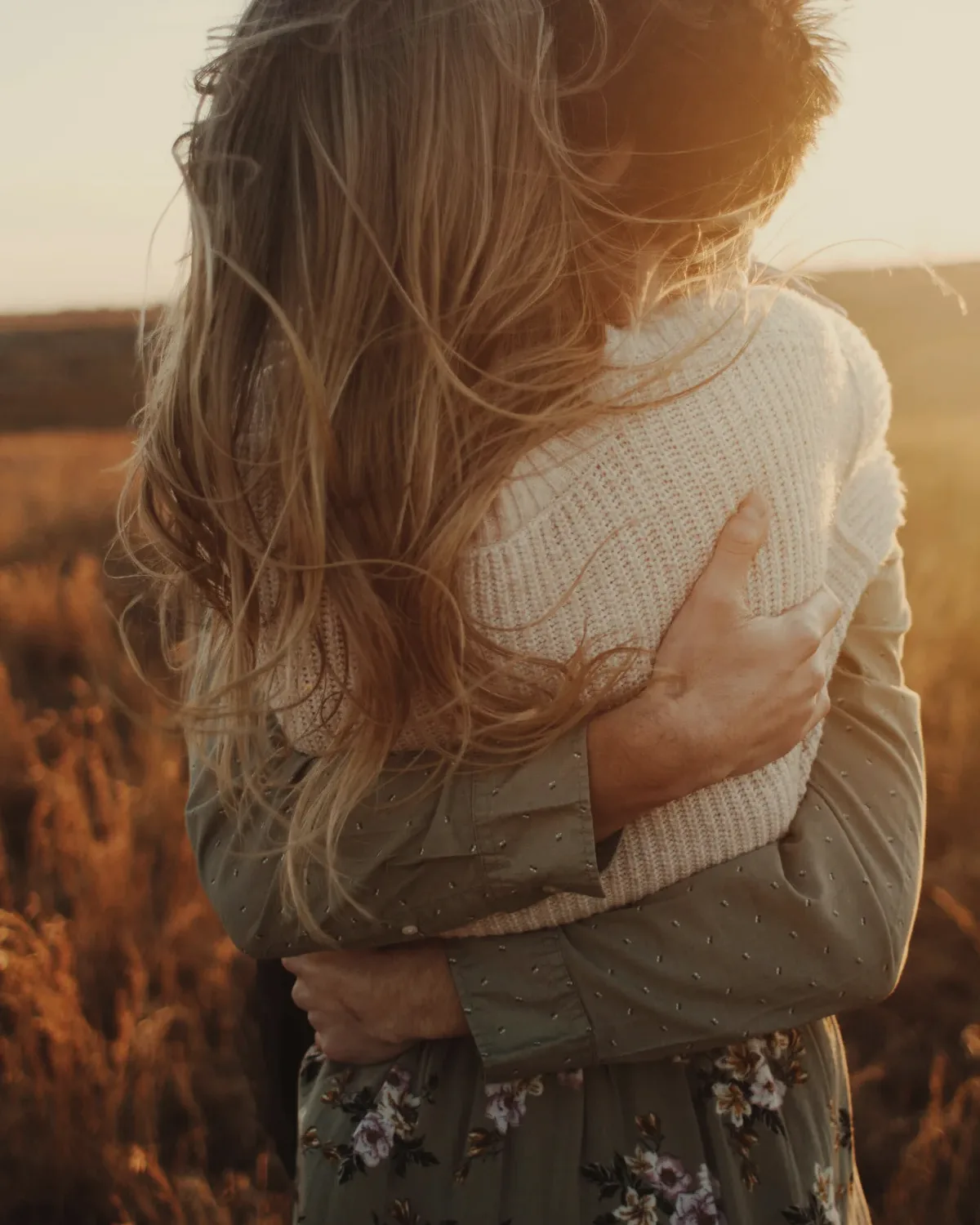 Pareja abrazada al atardecer en un campo, de espaldas